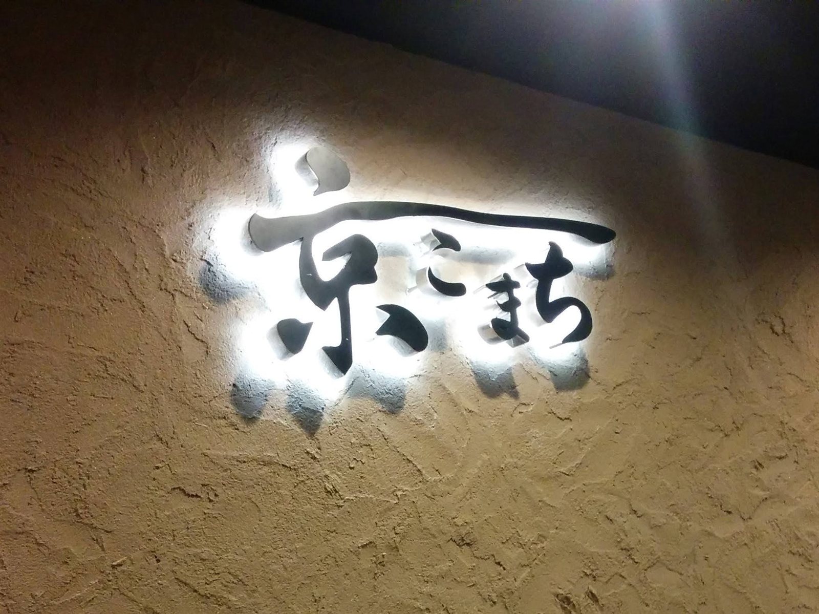 背面発光サインの夜間点灯（塗り壁に筆文字のシルエットが浮かぶ）