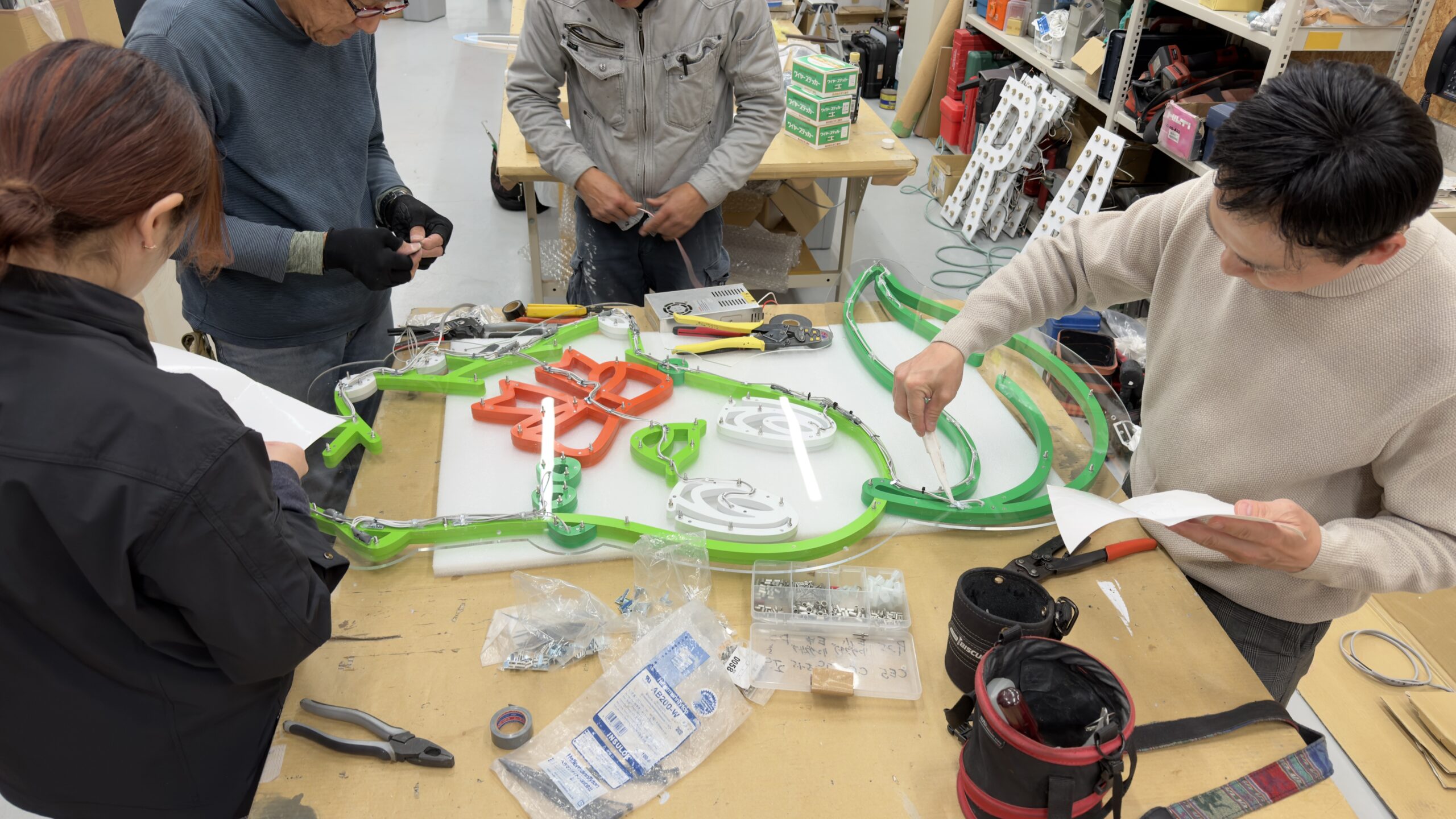 工房でネオンサインを組み立てるスタッフの作業風景 工具と取付金具